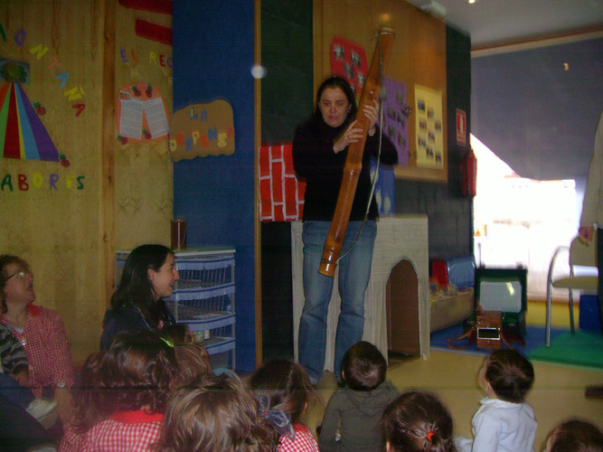 Chica explicando un instrumento musical a un grupo de niños y su profesora.