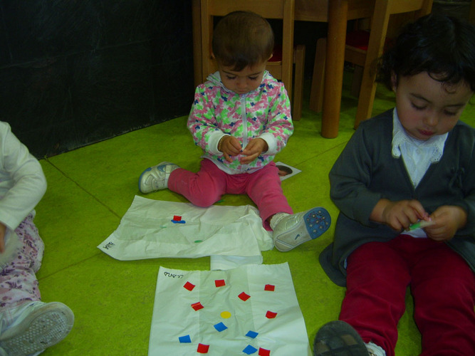 Niños jugando en el suelo con pegatinas de colores.