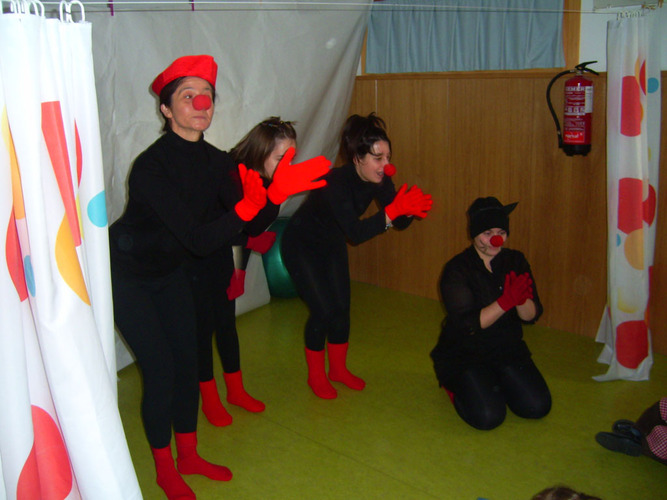 Profesoras disfrazadas de negro con guantes, calcetines y nariz roja, aplaudiendo.