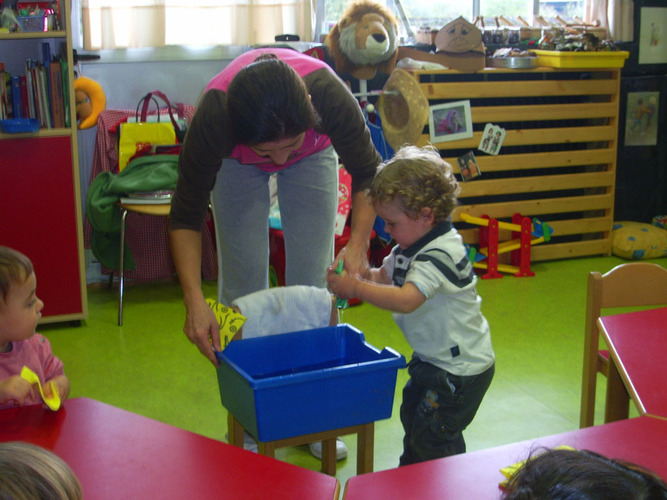 Profesora lavandole las manos a un niño en un cubo.