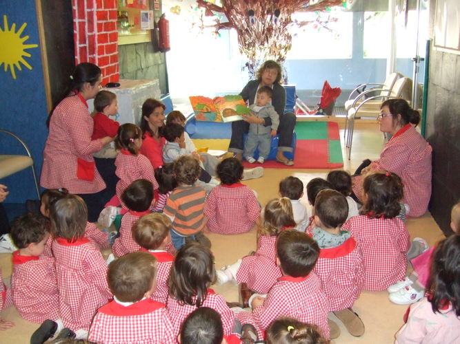 Profesora leyendo un libro para un grupo de niños y otras profesoras.