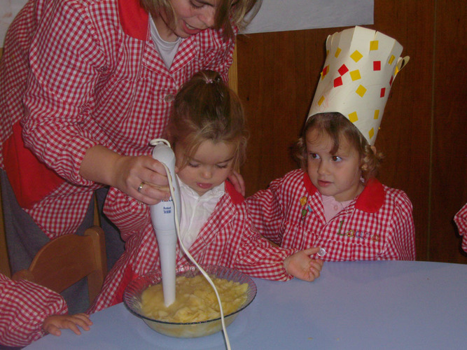 Profesora ayuda a una niña a triturar los trozos de manzana, zumo de limón y azúcar, usando la batidora.