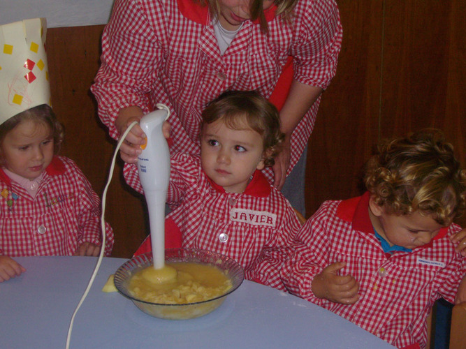 Profesora ayuda a un niño a triturar los trozos de manzana, zumo de limón y azúcar.