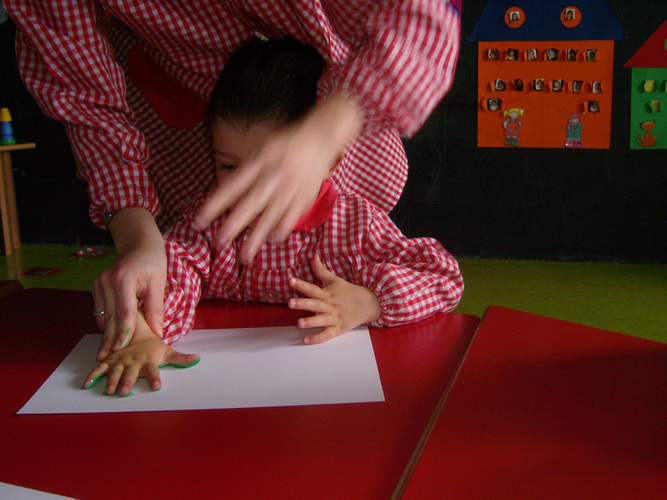 Profesora ayudando a un niño a marcar en un folio, la palma de la mano de color verde.
