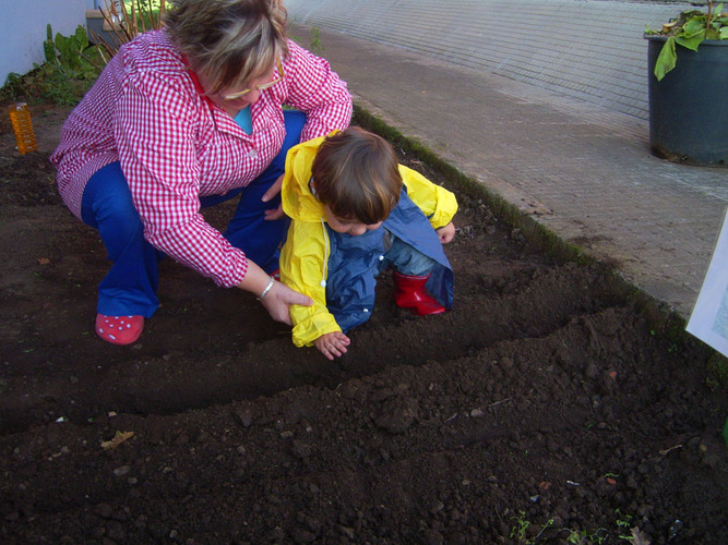 Profesora enseñando a un niño a plantar semillas en un huerto.