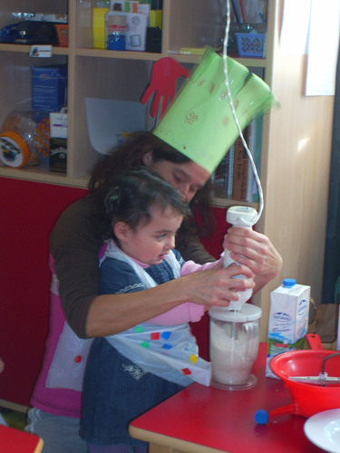 Profesora ayudando a una niña a triturar el contenido de un recipiente.