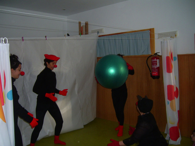 Profesoras disfrazadas de negro con guantes, calcetines y nariz roja, jugando con una pelota.