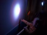 Un niño viendo la luz de una linterna proyectada sobre la pared blanca