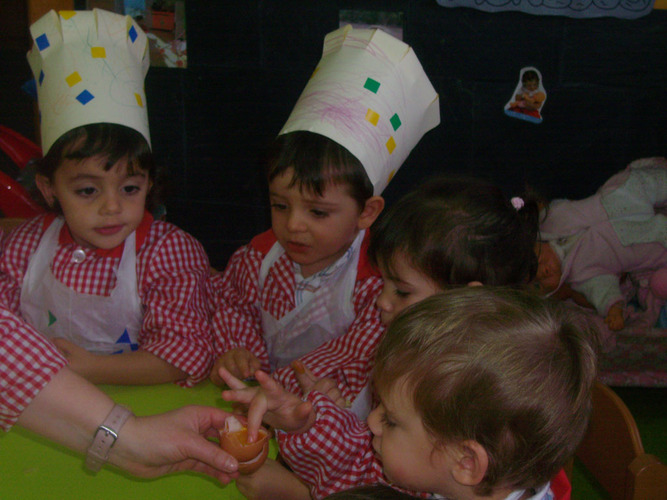 Niños con gorros de cocina, tocando la yema de un huevo.