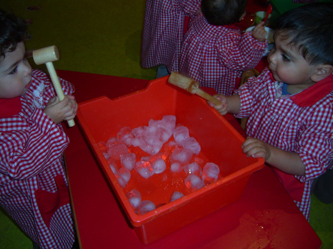 Niños jugando con los hielos de un cubo.