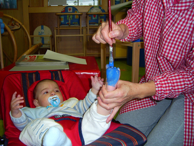 Profesora pintando de azul la planta del pie a un bebé.