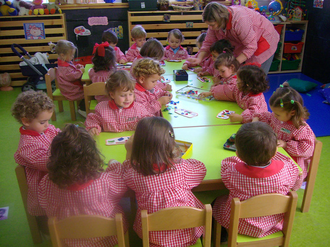 Grupo de niños junto a su profesora, sentados jugando.