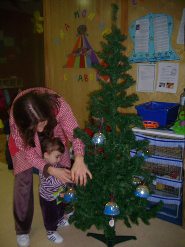 Niño ayudada por su porfesora a colocar adorno de navidad en un árbol.