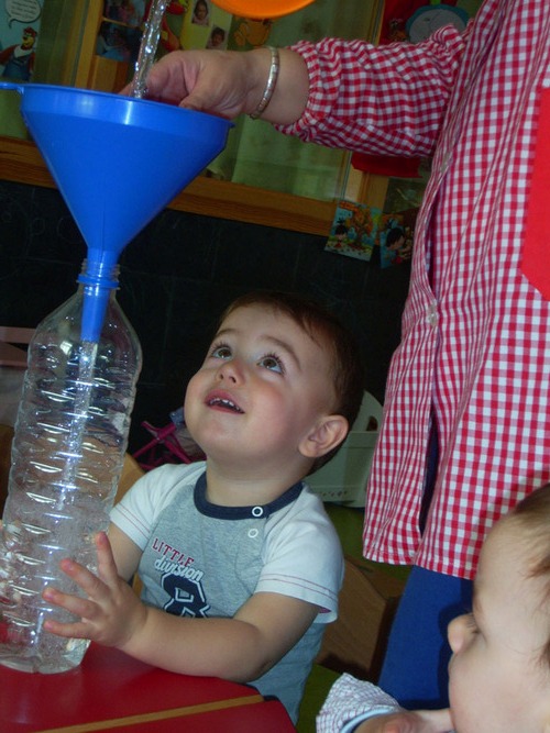 Niño mirando como su profesora echa agua en una botella através de un embudo.