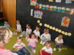 Varios niños sentados cantando y jugando con una educadora