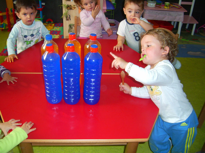 Niños pequeños mirando unas botellas de colores.