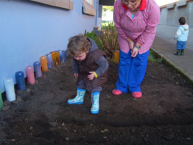 Profesora enseñando a un niño a plantar semillas en un huerto.
