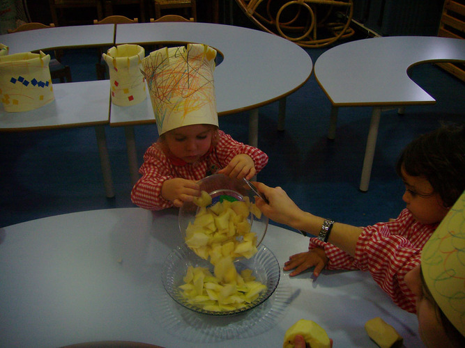 Niñas con gorros de cocineras volcando trozos de manzana en un recipiente.