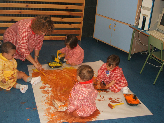 Niños muy pequeños pintando en un mural con su profesora.