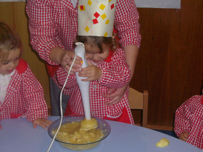 Profesora ayuda a una niña a triturar los trozos de manzana, zumo de limón y azúcar, usando la batidora.