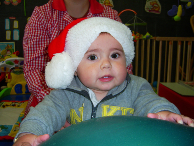 Niño muy pequeño posando con un gorro de Papa Noel y agarrado a una pelota verde gigante.
