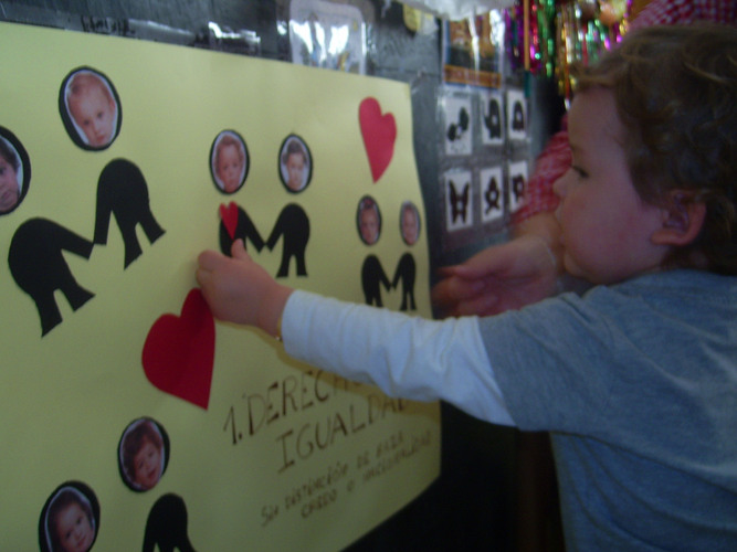 Niño pegando un corazón en un cartel sobre un monigote que tiene su foto.