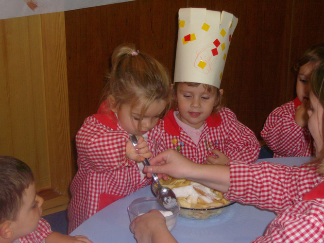 Una niña es ayudada a echar azucar en el recipiente con manzana y zumo de limón.
