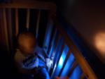 Niño dentro de la cuna, proyectado luz azul con una linterna sobre la pared