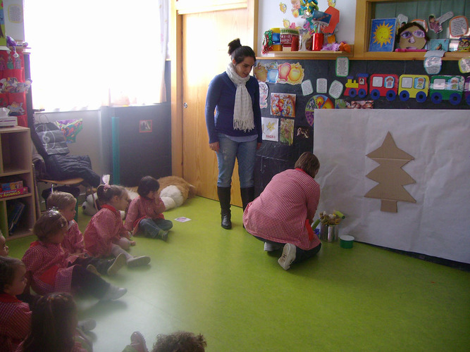 Niños sentados, mirando a sus profesoras preparar el material para decorar un mural.