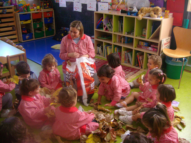 Grupo de niños y su profesora, jugando con hojas de árboles.