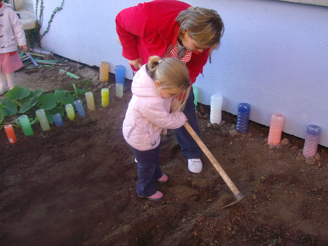 Profesora enseñando a una niña a arar un huerto.
