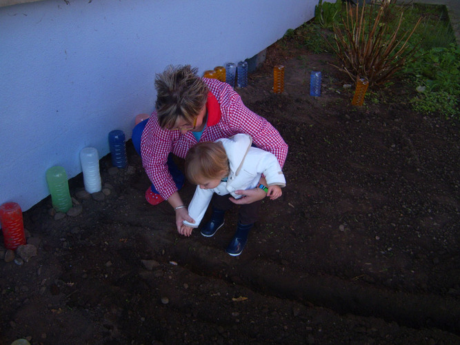 Profesora enseñando a una niña a plantar semillas en un huerto.
