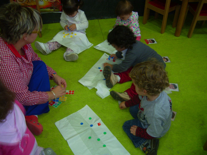 Niños junto a su profesora jugando en el suelo con pegatinas de colores.