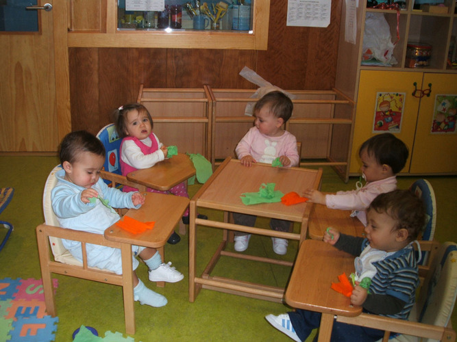 Grupo de niños sentados en unas tronas, jugando con unos papeles de colores.