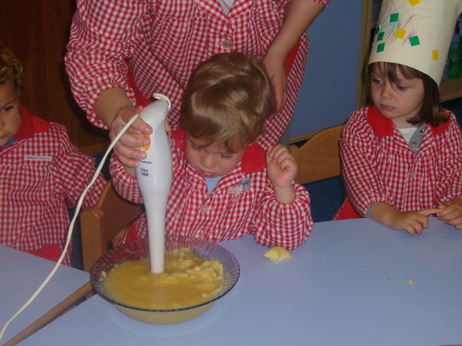 Profesora ayuda a un niño a triturar los trozos de manzana, zumo de limón y azúcar, usando la batidora.