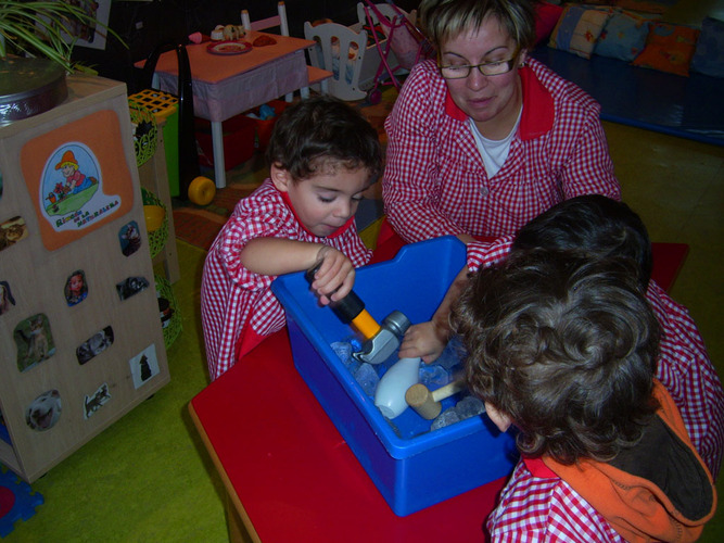Niños jugando con los hielos de un cubo, junto a su profesora.