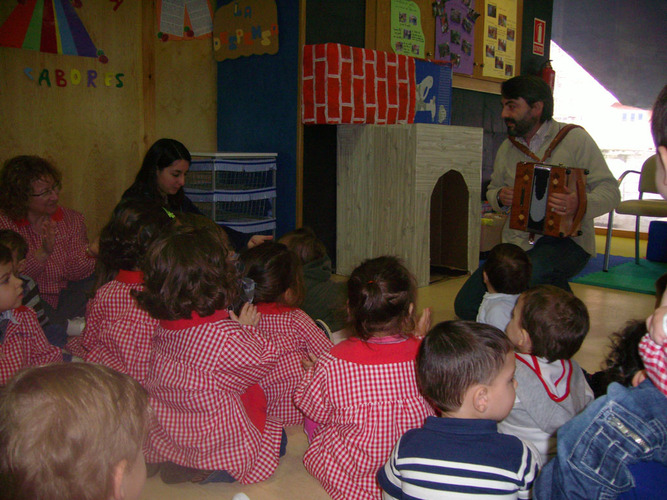 Chico tocando acordeón, mientras un grupo de niños y profesoras dan palmas.