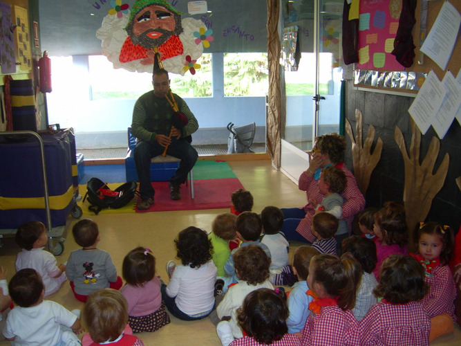 Chico tocando la gaita para un grupo de niños y su profesora.