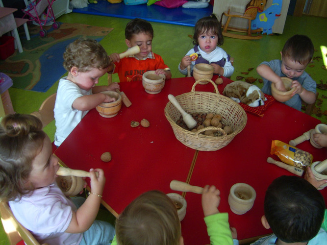 Grupo de niños machacando en unos morteros avellanas y nueces.