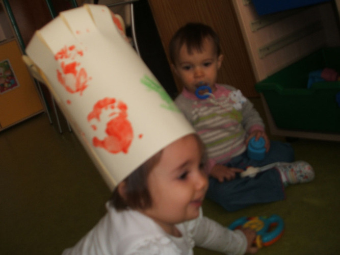 Niña con gorro de cocinero, jungando mientras otro niño con chupete la mira.