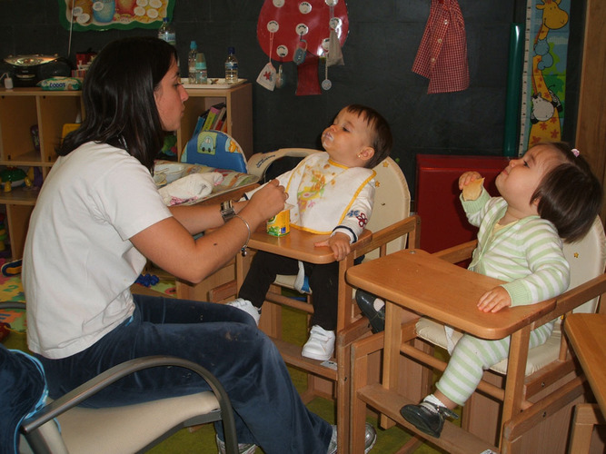 Profesora dando de comer a dos bebés en unas tronas.