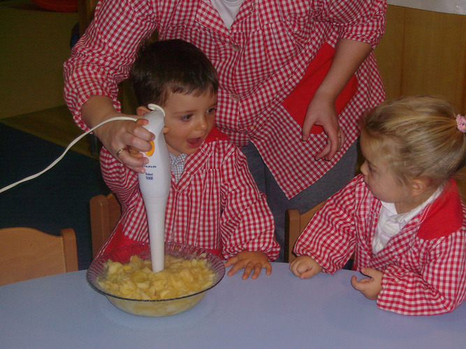 Profesora ayuda a un niño a triturar los trozos de manzana, zumo de limón y azúcar, usando la batidora.