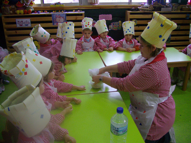 Grupo de niños y su profesora con gorros de cocina.