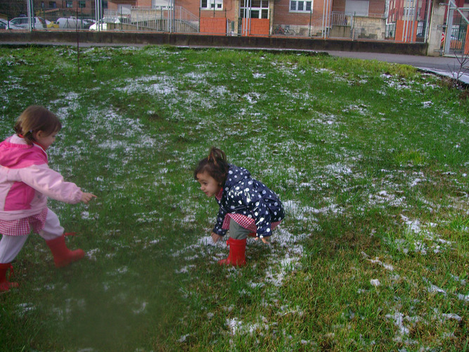 Dos niñas jutando con el granizo de un prado.