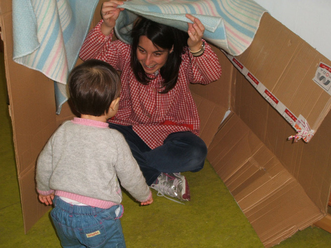 Profesora saliendo de debajo de una manta para hacer reir a una niña.