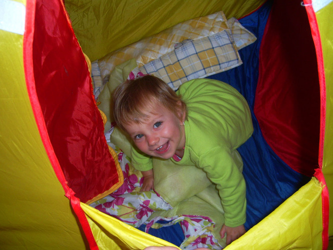 Niña jugando dentro de una tienda de campaña de colores.