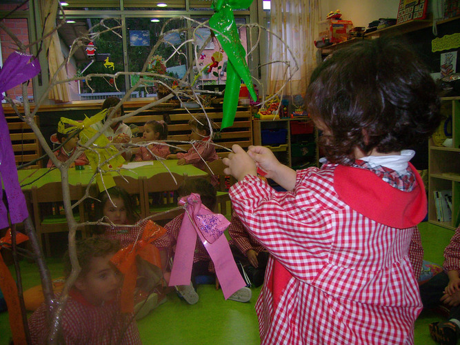 Niña decorando un árbol con lazos de colores.