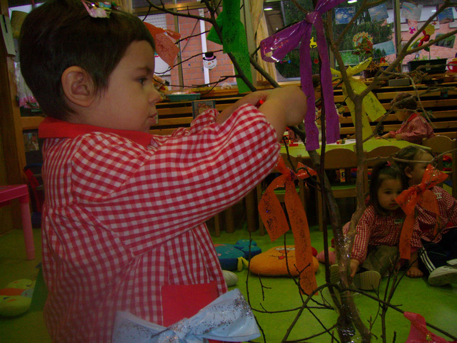 Niño decorando un árbol con lazos de colores.