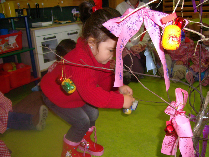 Niña decorando un árbol con bolas de colores.