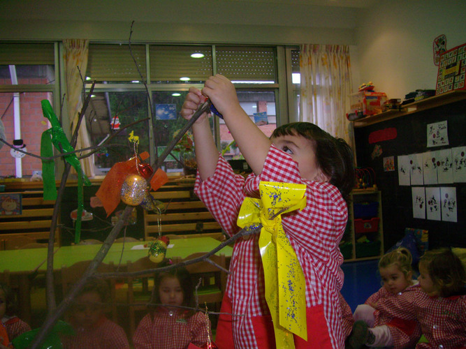 Niño decorando un árbol con lazos de colores.